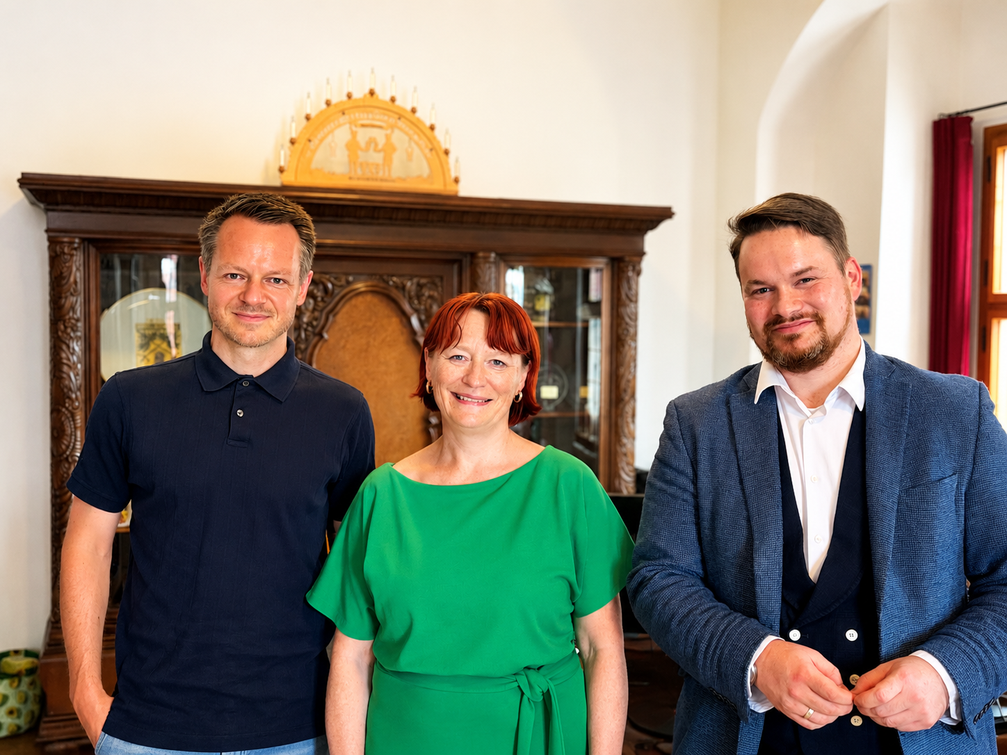 KI generiert: Das Bild zeigt drei Personen, die in einem Raum mit antiker Einrichtung stehen und in die Kamera lächeln. Der Hauptinhalt des Bildes ist die Darstellung der drei Personen vor einem alten Schrank mit einer goldenen Krone darauf.