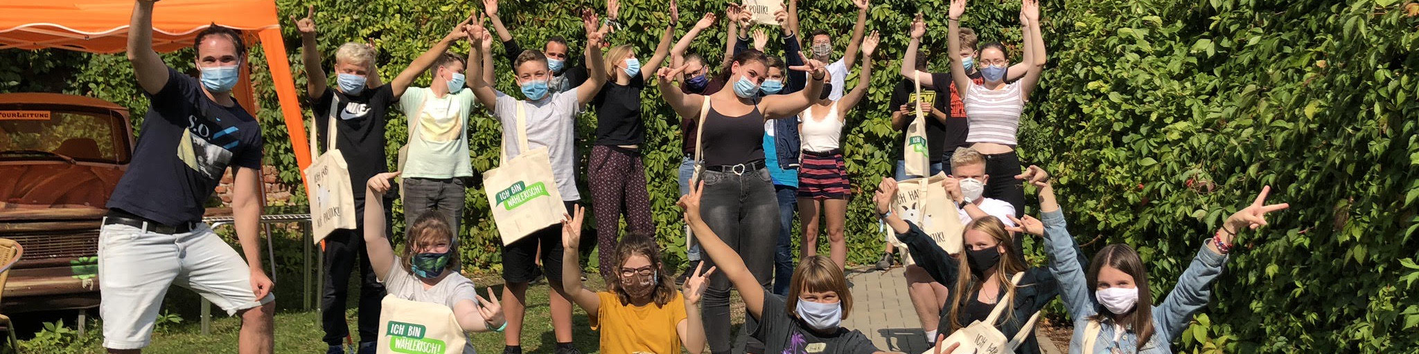 KI generiert: Das Bild zeigt eine Gruppe von Menschen, die draußen in einem grünen Bereich stehen und sich freudig mit erhobenen Armen präsentieren, wobei viele von ihnen Gesichtsmasken tragen und einige T-Shirts mit dem Aufdruck "Greenpeace" tragen. Der Hauptinhalt des Bildes ist eine fröhliche Gruppe von Greenpeace-Aktivisten, die sich versammelt haben, um ihre Unterstützung für die Umweltorganisation zu zeigen.