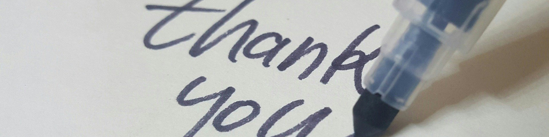 KI generiert: Das Bild zeigt einen Ausschnitt eines handgeschriebenen "thank you" auf Papier mit einem blauen Stift, der gerade den Text schreibt. Der Hauptinhalt des Bildes ist der Ausdruck von Dankbarkeit.
