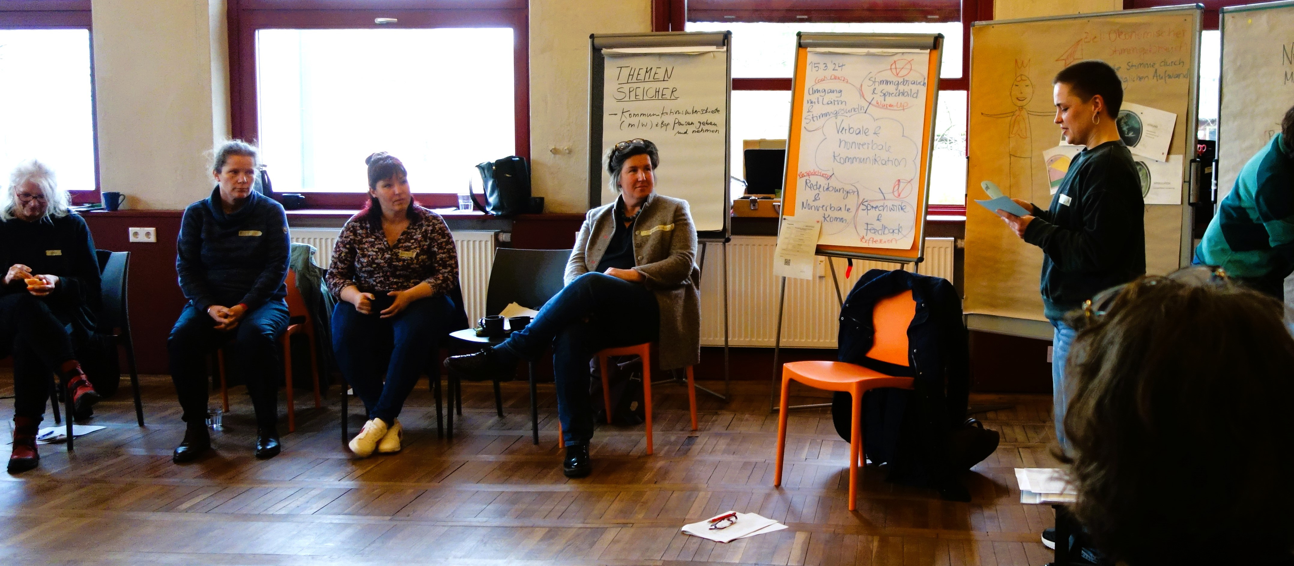 KI generiert: Das Bild zeigt eine Gruppe von Personen in einem Seminarraum, wobei eine Person vorne steht und eine Präsentation hält, während die anderen auf Stühlen sitzen und zuhören. Der Hauptinhalt des Bildes ist eine Schulung oder ein Workshop.