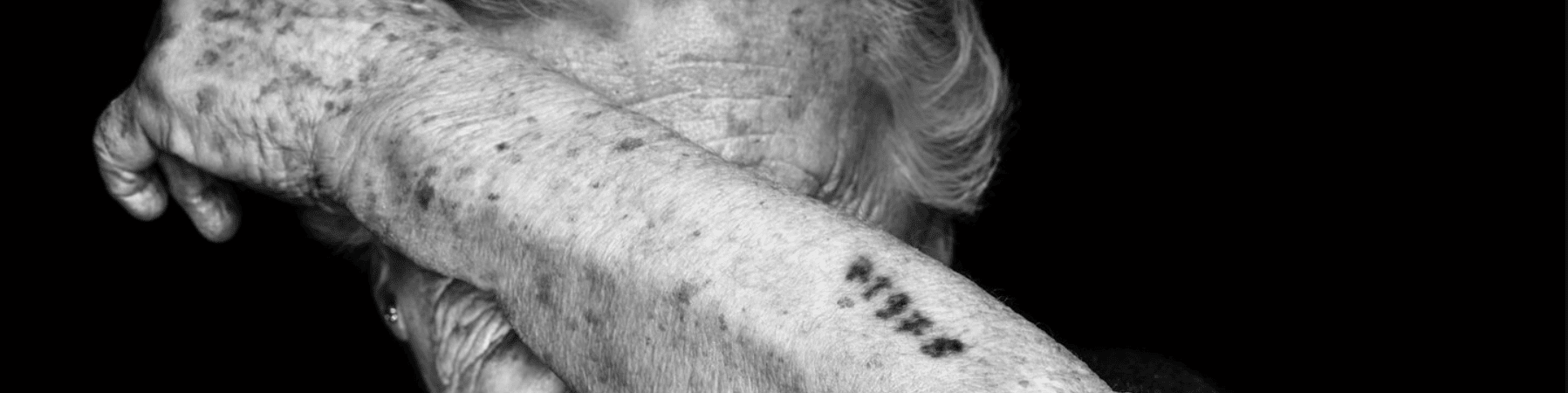 KI generiert: Das Bild zeigt den Unterarm einer älteren Person mit sichtbaren Altersflecken und einer tätowierten Zahlenfolge. Der Hauptinhalt des Bildes ist die Tätowierung, die an die Nummern erinnert, die während des Holocaust in Konzentrationslagern verwendet wurden.