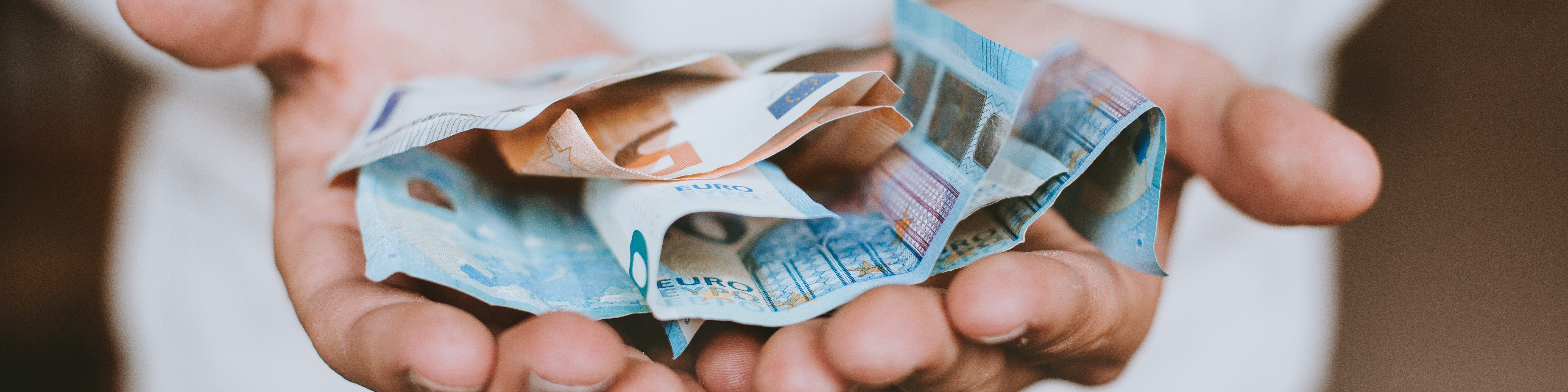 KI generiert: Das Bild zeigt zwei Hände, die mehrere zerknüllte Euro-Banknoten halten. Der Hauptinhalt des Bildes ist Geld, genauer gesagt Euro-Geldscheine.