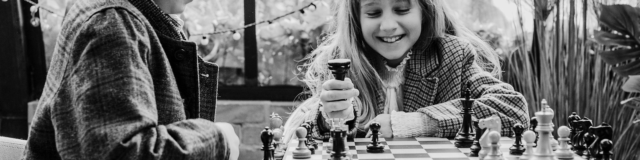 KI generiert: Das Bild zeigt zwei Personen, die an einem Tisch sitzen und Schach spielen, wobei eine junge Person im Vordergrund einen Zug macht. Der Hauptinhalt des Bildes ist das Schachspiel zwischen den beiden Personen.