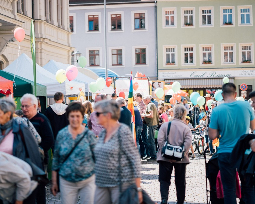 KI generiert: Das Bild zeigt eine belebte Straßenveranstaltung mit vielen Menschen, bunten Dekorationen und Spielstationen für Kinder. Im Mittelpunkt stehen Familien, die gemeinsam verschiedene Aktivitäten genießen.