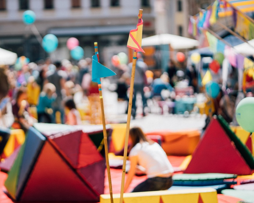 KI generiert: Das Bild zeigt eine Gruppe von Menschen, die auf Bänken sitzen und einer Veranstaltung im Freien zuhören. Der Hauptinhalt ist eine Gemeinschaftsveranstaltung, bei der Menschen verschiedenen Alters zusammenkommen.