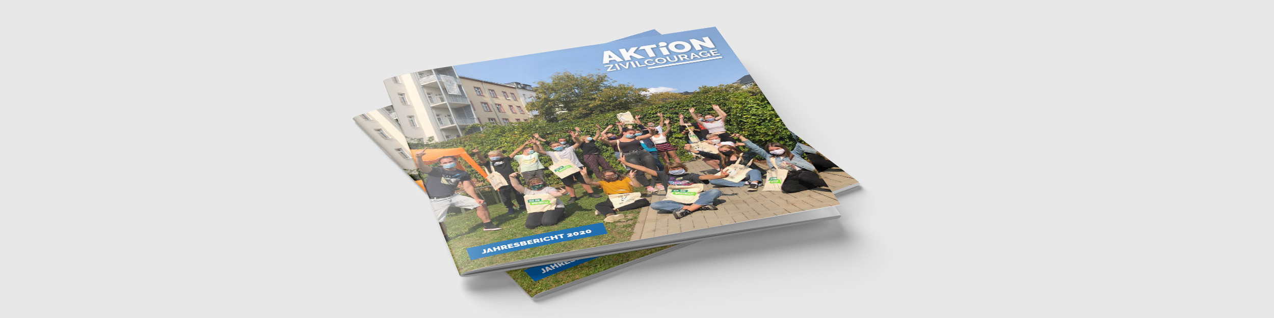 KI generiert: Das Bild zeigt mehrere Exemplare eines Jahresberichts mit dem Titel "Aktion Zivilcourage" auf einem Stapel. Der Hauptinhalt des Bildes ist der Jahresbericht selbst, der auf dem Cover eine Gruppe von Menschen in einer entspannten, geselligen Atmosphäre im Freien zeigt.