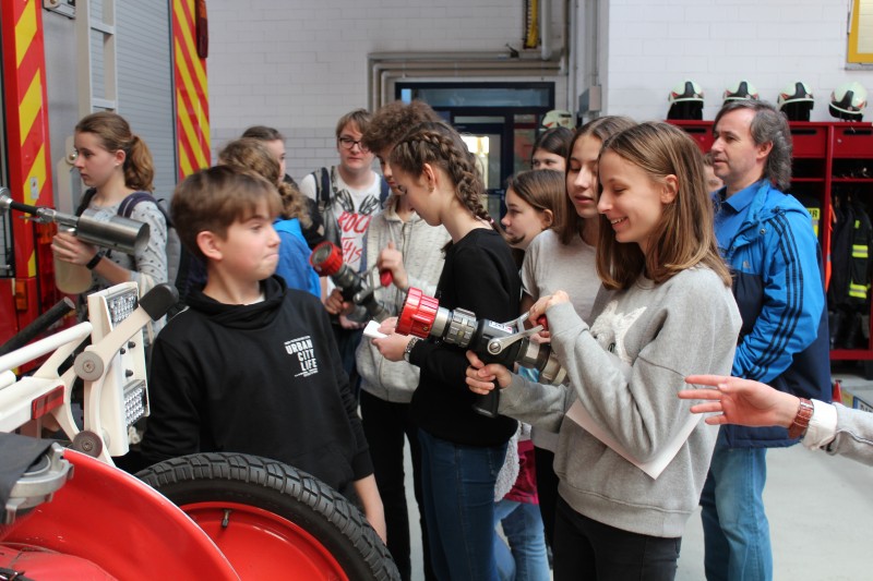 KI generiert: Das Bild zeigt eine Gruppe von Jugendlichen und Erwachsenen in einer Feuerwehrwache, die sich mit Feuerlöschern vertraut machen. Der Hauptinhalt des Bildes ist eine praktische Brandschutzübung oder eine Führung durch die Feuerwehr.