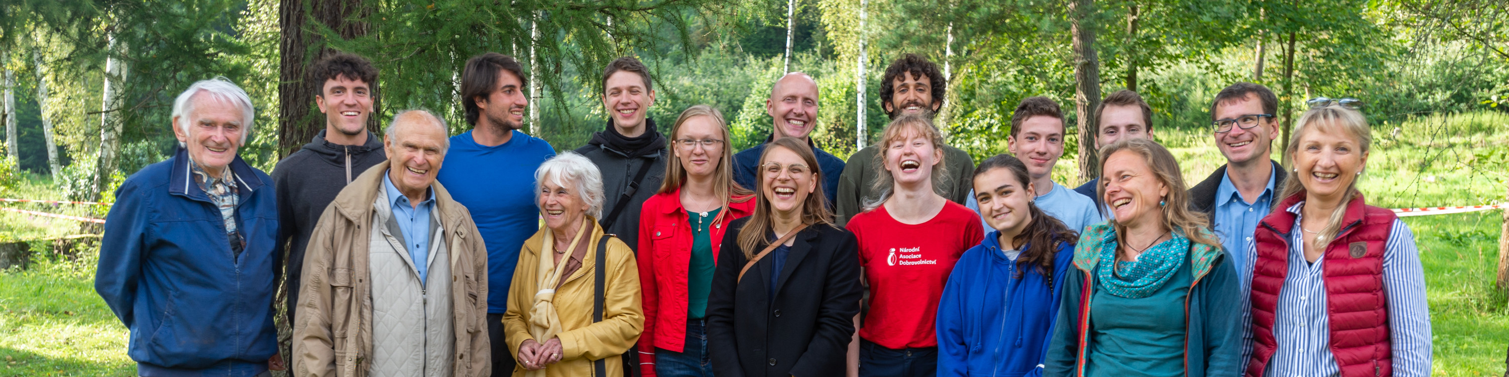 KI generiert: Das Bild zeigt eine Gruppe von Menschen, die in einer natürlichen Umgebung, möglicherweise einem Wald oder Park, zusammenstehen und lächeln. Der Hauptinhalt des Bildes ist die Darstellung einer fröhlichen und vielfältigen Gruppe in einer Outdoor-Umgebung.