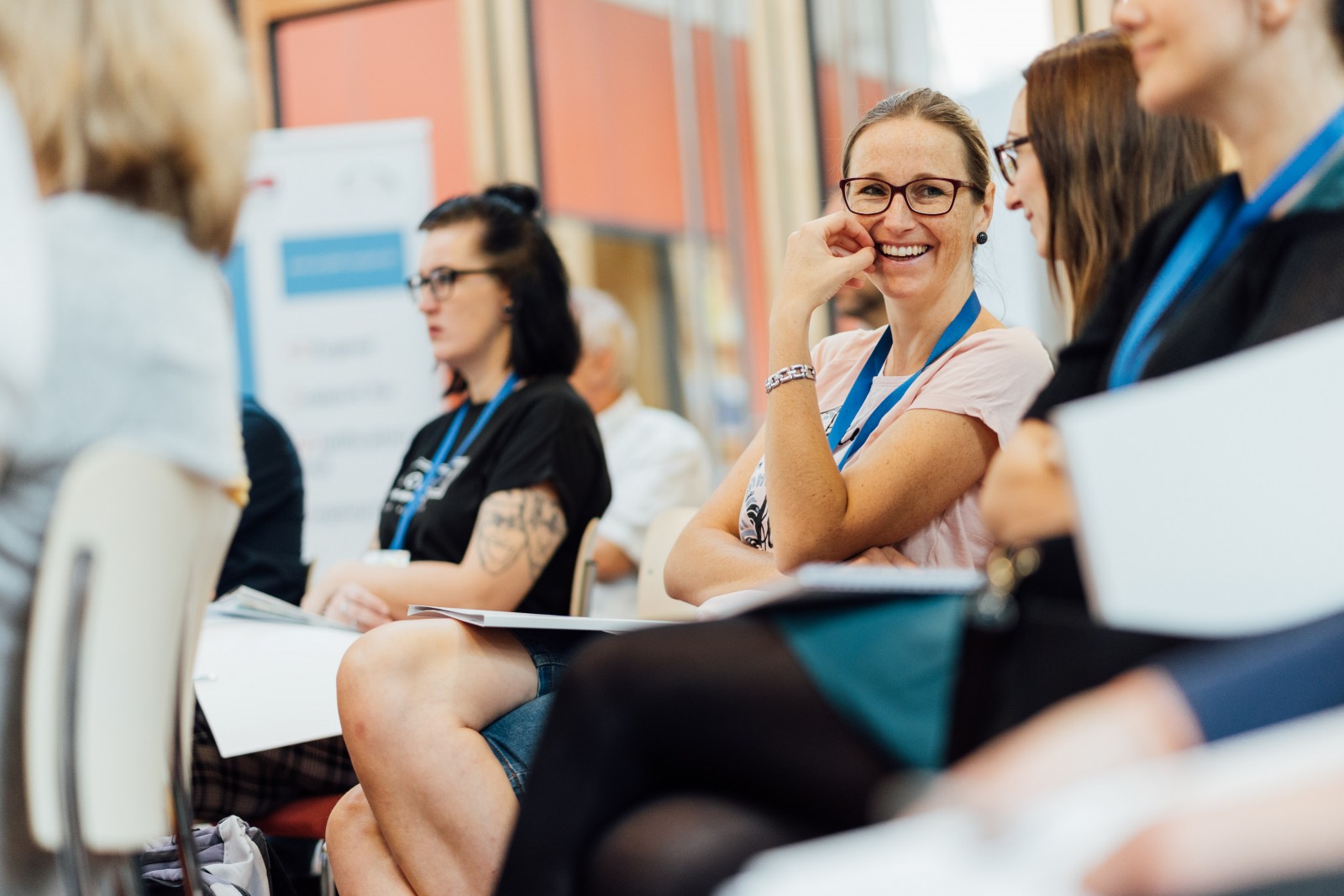 KI generiert: Das Bild zeigt eine Gruppe von Personen, die in einer informellen Sitzung oder einem Workshop zusammenkommen. Die Teilnehmer halten Notizblöcke und tragen Namensschilder, was auf eine organisierte Veranstaltung oder Konferenz hindeutet.