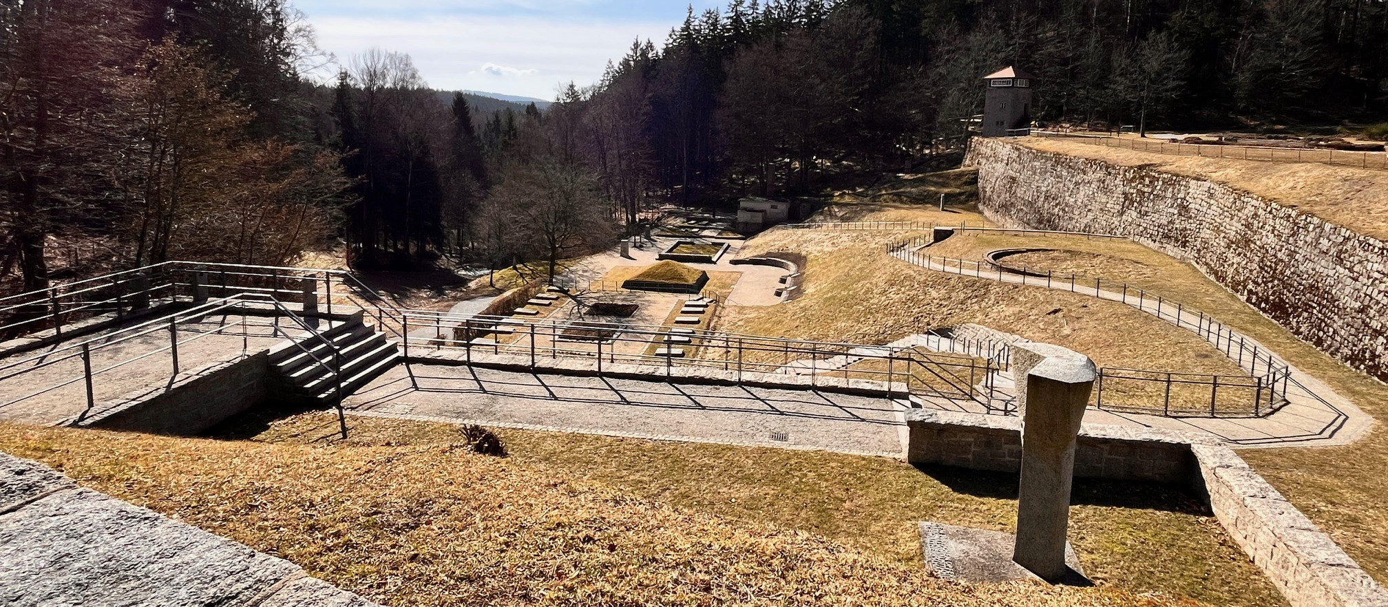KI generiert: Das Bild zeigt eine historische Festungsanlage mit trockenen Gräben und Steinmauern, umgeben von einem Wald. Im Hintergrund ist ein kleiner Turm oder Pavillon zu sehen.