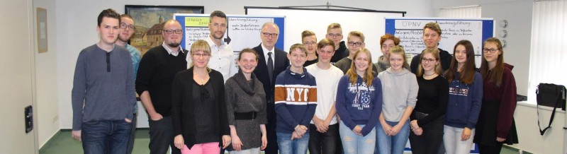 KI generiert: Das Bild zeigt eine Gruppe von Jugendlichen und Erwachsenen, die gemeinsam in einem Raum stehen und posieren. Es scheint sich um eine offizielle Veranstaltung oder ein Treffen zu handeln, möglicherweise im Bildungs- oder Gemeinschaftskontext.