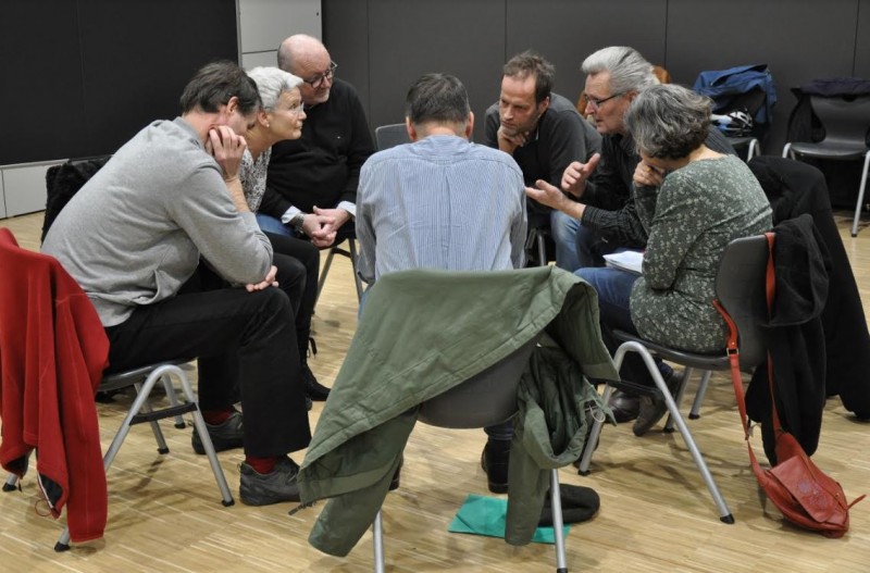 KI generiert: Das Bild zeigt eine Gruppe von Personen, die in einem Kreis sitzen und sich angeregt unterhalten. Der Hauptinhalt des Bildes ist eine Diskussion oder ein Meeting in einem informellen Rahmen.