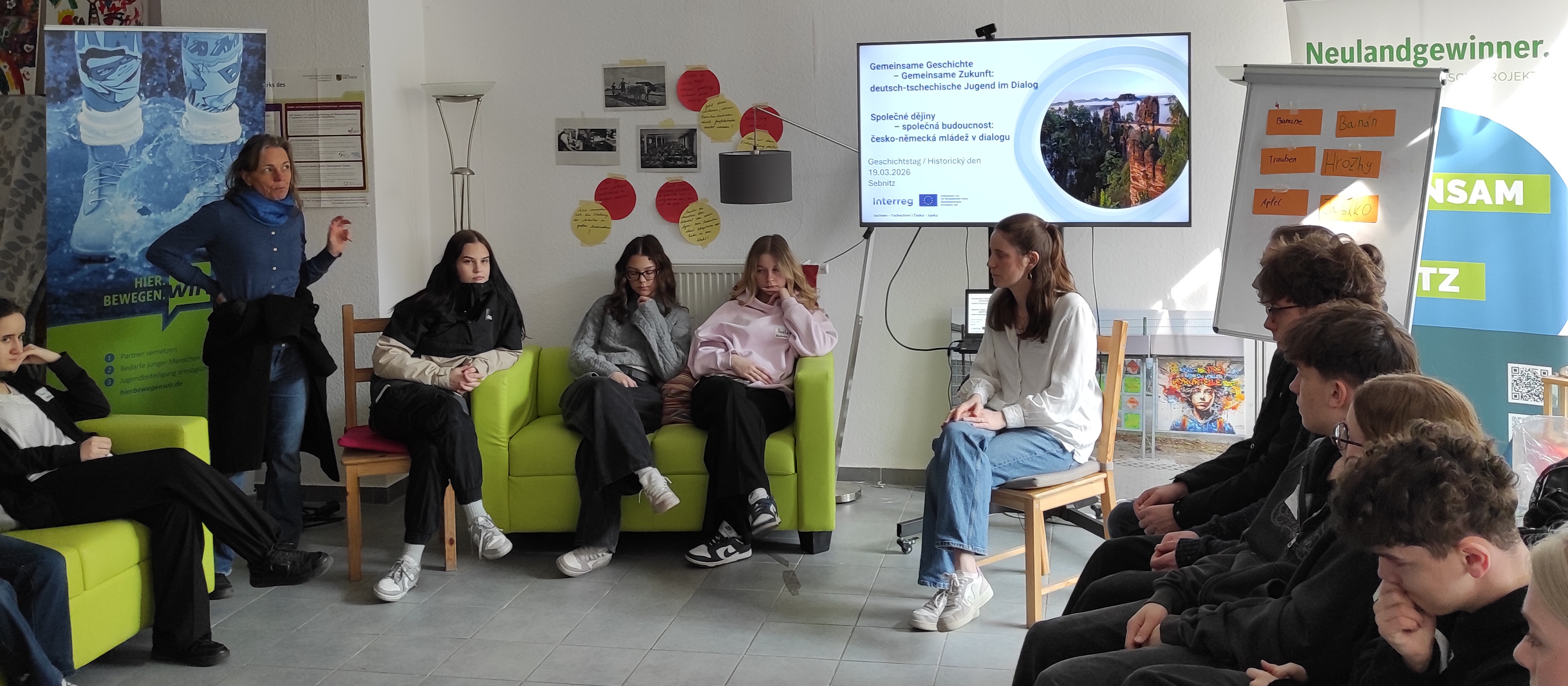 KI generiert: Das Bild zeigt eine Gruppe von Jugendlichen, die in einem Raum mit bunten Wänden und Postern sitzen und einer Präsentation oder Diskussion folgen. Der Hauptinhalt des Bildes ist eine Bildungsveranstaltung oder ein Workshop, bei dem Themen wie Nachhaltigkeit oder Umweltbewusstsein behandelt werden.
