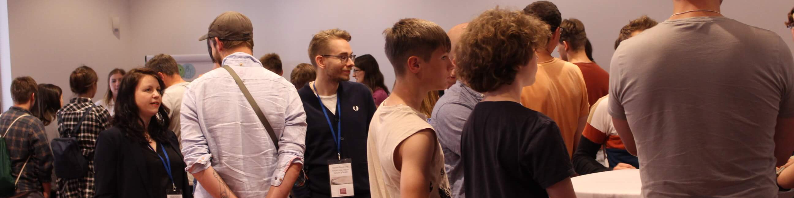 KI generiert: Das Bild zeigt eine Gruppe von Personen, die in einem Innenraum stehen und sich unterhalten. Es scheint sich um eine informelle Zusammenkunft oder ein Netzwerktreffen zu handeln, bei dem die Teilnehmer in Gespräche vertieft sind.