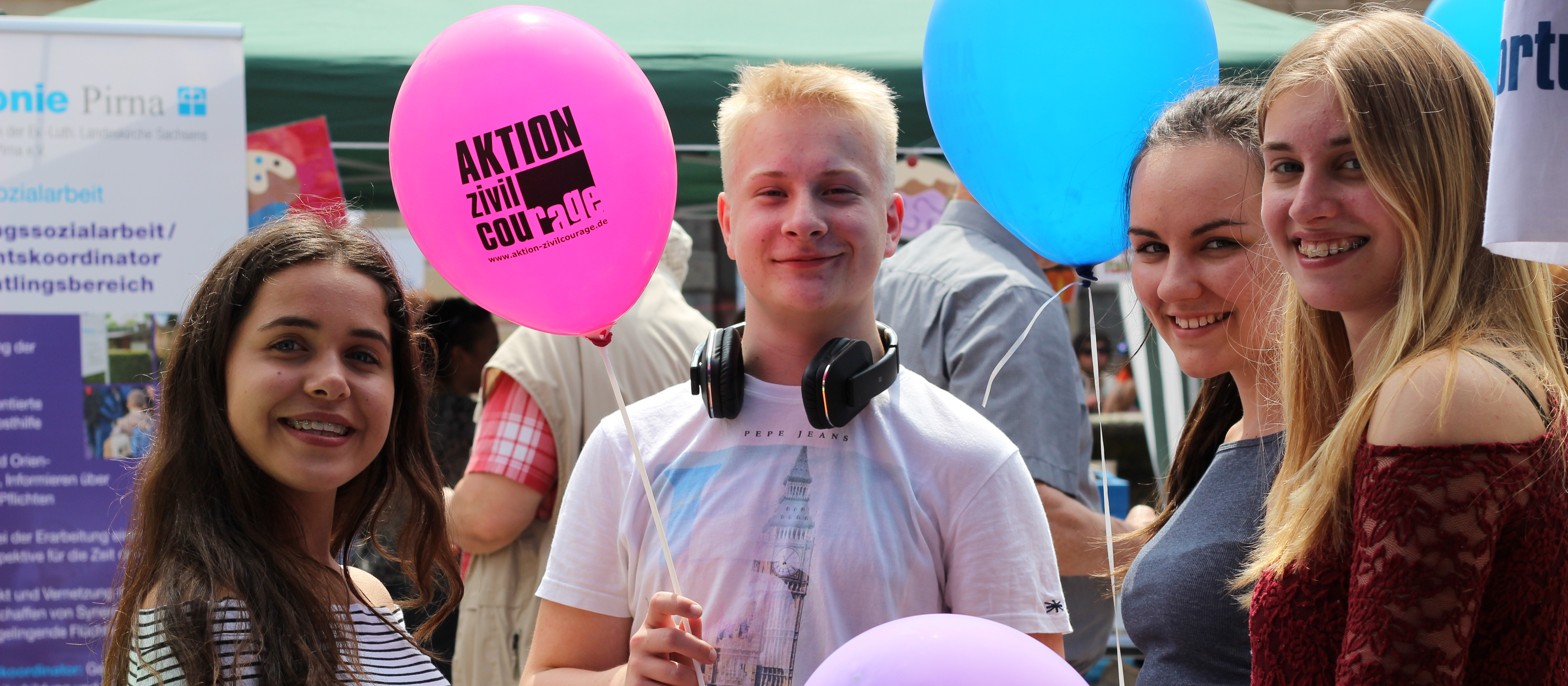 KI generiert: Das Bild zeigt eine Gruppe junger Menschen auf einer Veranstaltung, die Ballons in den Farben Pink und Blau halten, wobei einer der Ballons die Aufschrift "AKTION Zivilcourage" trägt. Der Hauptinhalt des Bildes ist die Darstellung von Engagement und Gemeinschaftsgefühl, möglicherweise im Rahmen einer Kampagne oder eines Events zur Förderung von Zivilcourage.