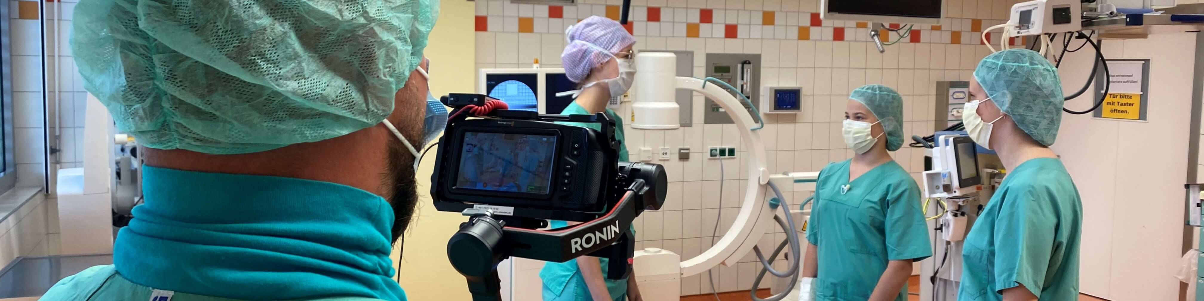 KI generiert: Das Bild zeigt eine Gruppe von medizinischem Personal in einem Operationssaal, die sich auf eine Operation vorbereiten. Im Vordergrund ist eine Person mit einer Kameraausrüstung zu sehen, die möglicherweise die Operation aufzeichnet.
