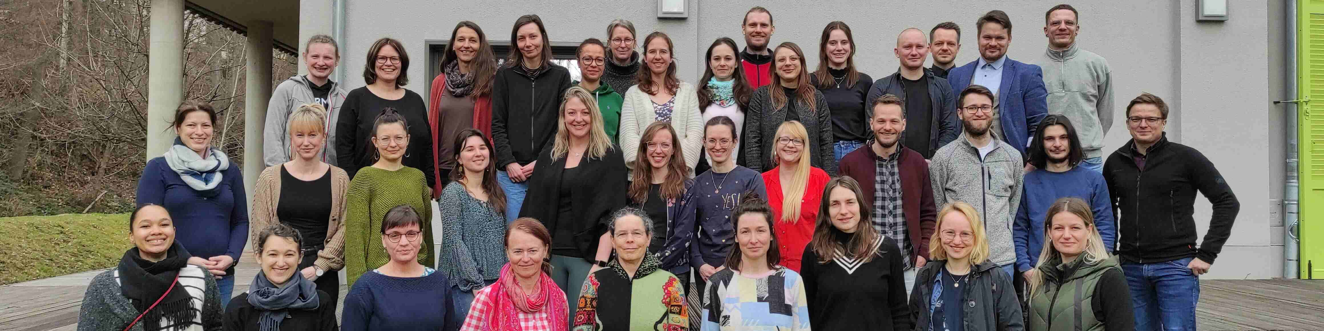 KI generiert: Das Bild zeigt eine große Gruppe von Menschen, die vor einem Gebäude posieren. Der Hauptinhalt des Bildes ist eine Gruppenfotografie, die vermutlich an einem offiziellen oder geselligen Anlass aufgenommen wurde.