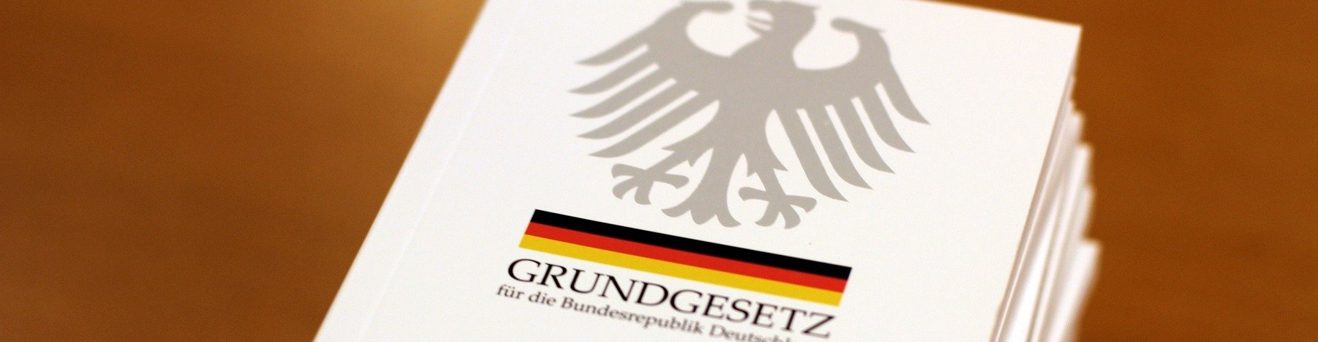 KI generiert: Das Bild zeigt eine Ausgabe des Grundgesetzes für die Bundesrepublik Deutschland mit dem Bundesadler und einer schwarz-rot-goldenen Flagge auf dem Umschlag. Der Hauptinhalt ist das deutsche Grundgesetzbuch.
