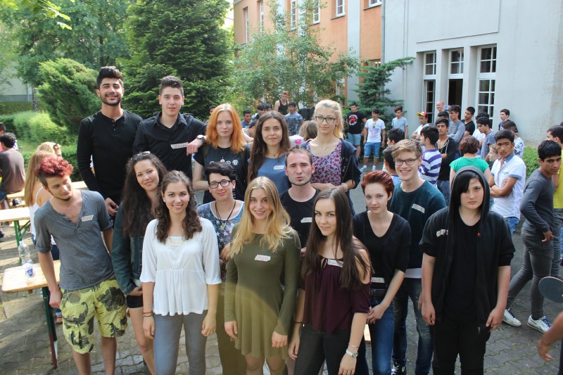 KI generiert: Das Bild zeigt eine Gruppe junger Menschen, die draußen vor einem Gebäude stehen und sich für ein Gruppenfoto versammelt haben. Der Hauptinhalt des Bildes ist die Gruppe von Personen, die gemeinsam posieren.