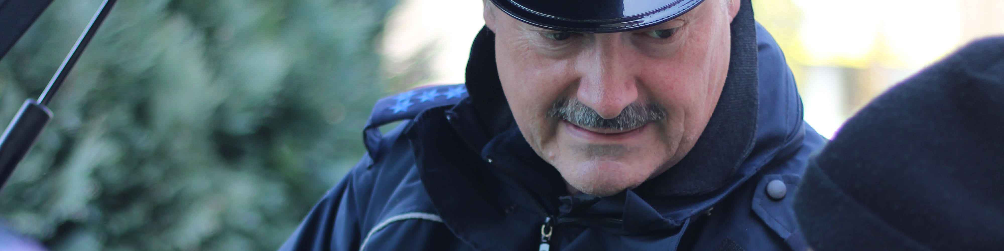 KI generiert: Das Bild zeigt einen Mann mit einem dunklen Hut und einer Jacke, der sich leicht nach vorne beugt. Der Hauptinhalt des Bildes ist das Porträt des Mannes, der in einer scheinbar natürlichen Umgebung steht.