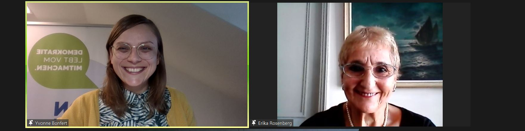 KI generiert: Das Bild zeigt zwei lächelnde Frauen in einer Videokonferenz, wobei eine vor einem Plakat mit der Aufschrift "DEMOKRATIE LEBT VOM MITMACHEN" sitzt. Der Hauptinhalt des Bildes ist die Darstellung einer virtuellen Interaktion oder eines Gesprächs zwischen den beiden Personen.