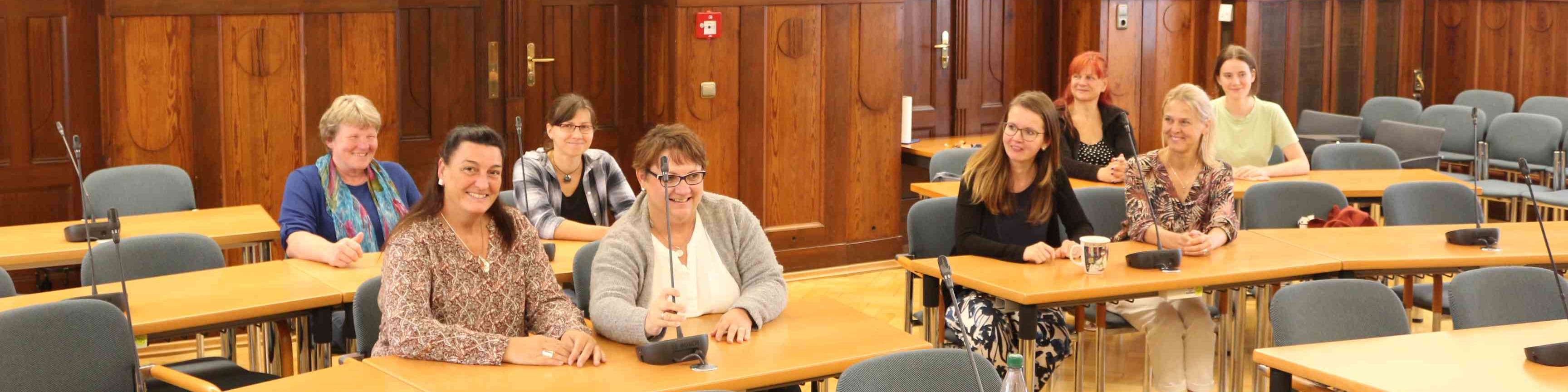 KI generiert: Das Bild zeigt eine Gruppe von Personen, die in einem Konferenzraum an langen Tischen sitzen. Der Hauptinhalt des Bildes ist eine Besprechung oder ein Seminar in einem formellen Umfeld.