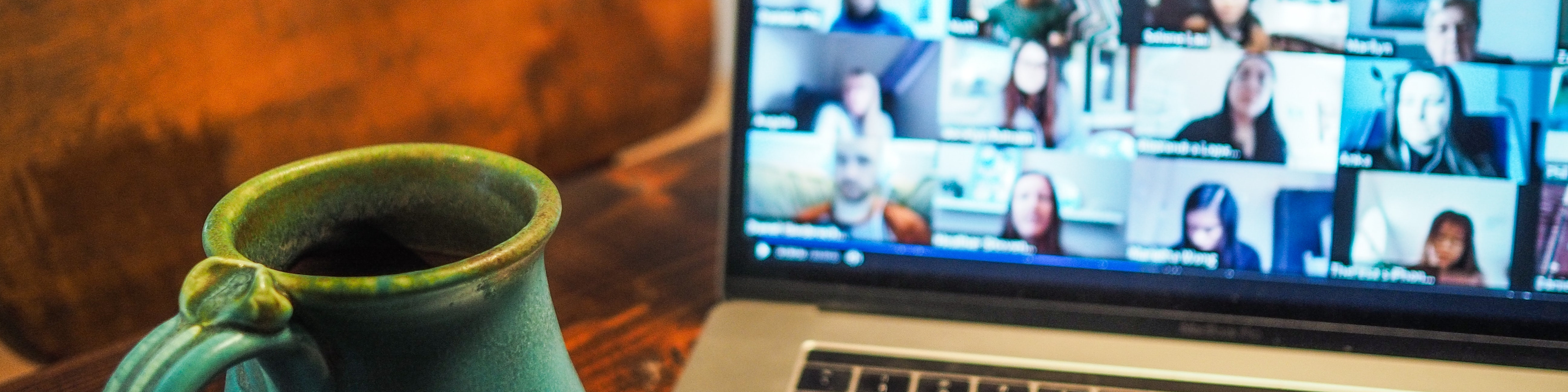 KI generiert: Das Bild zeigt einen Laptop mit einer laufenden Videokonferenz, bei der mehrere Personen auf dem Bildschirm zu sehen sind. Im Vordergrund steht eine grüne Tasse, möglicherweise mit einem heißen Getränk.