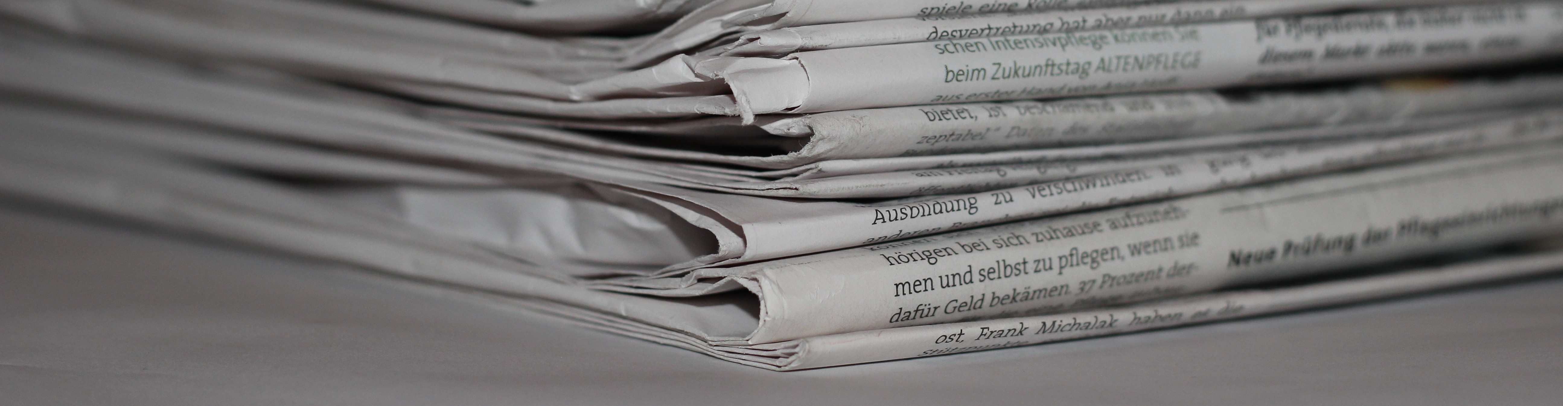 KI generiert: Das Bild zeigt einen Stapel von gefalteten Zeitungen, auf denen Textabschnitte zu erkennen sind. Der Fokus liegt auf den Kanten und den gedruckten Wörtern der Zeitungen.