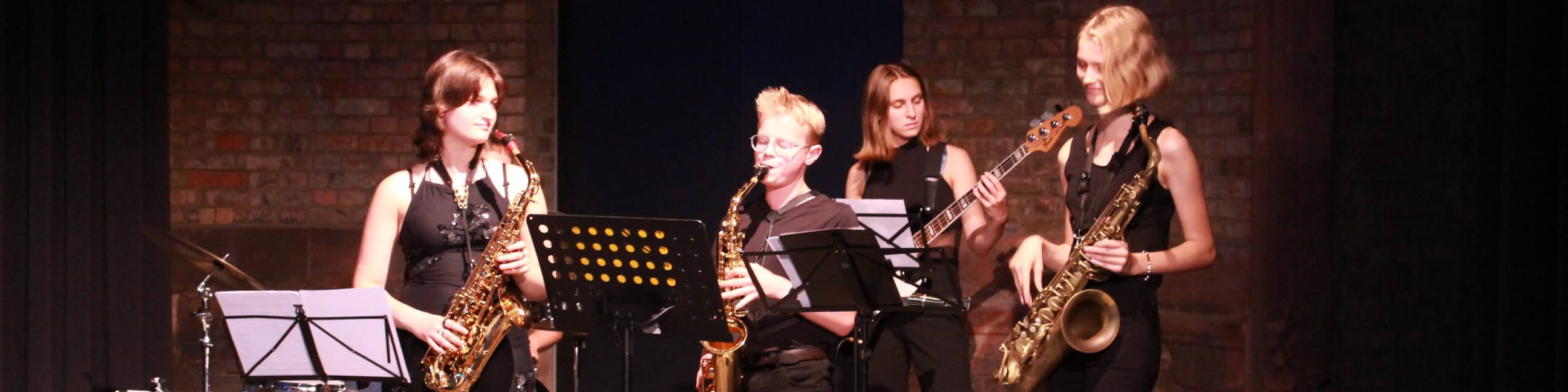 KI generiert: Das Bild zeigt eine Gruppe von vier Musikern auf einer Bühne, die Saxophone und eine E-Gitarre spielen. Der Hauptinhalt des Bildes ist ein Live-Auftritt einer Musikband.