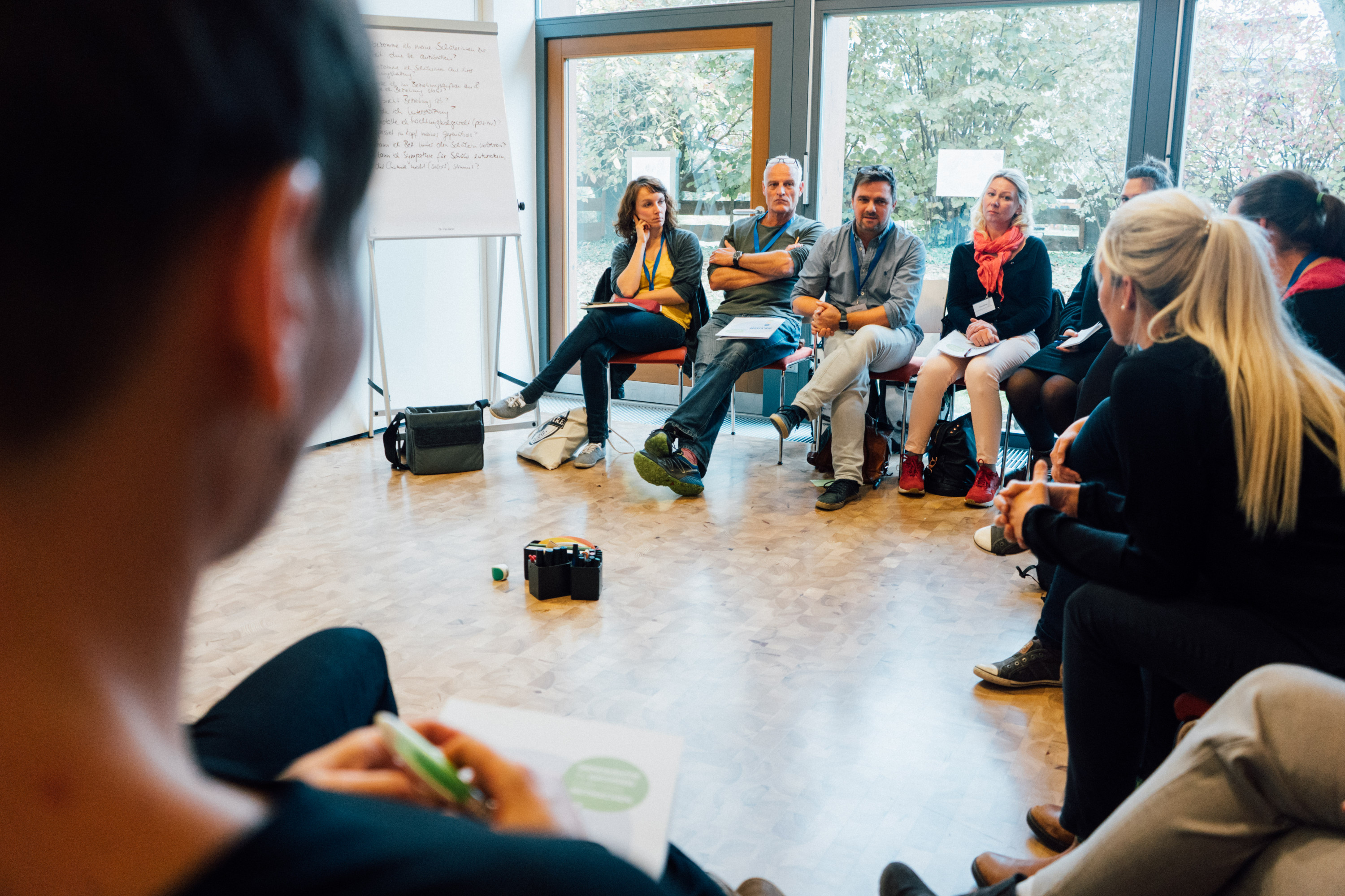 KI generiert: Das Bild zeigt eine Gruppe von Personen, die in einem Kreis sitzen und sich in einer Besprechung oder einem Workshop befinden. Der Hauptinhalt des Bildes ist eine interaktive Sitzung oder Diskussion in einem professionellen oder pädagogischen Umfeld.
