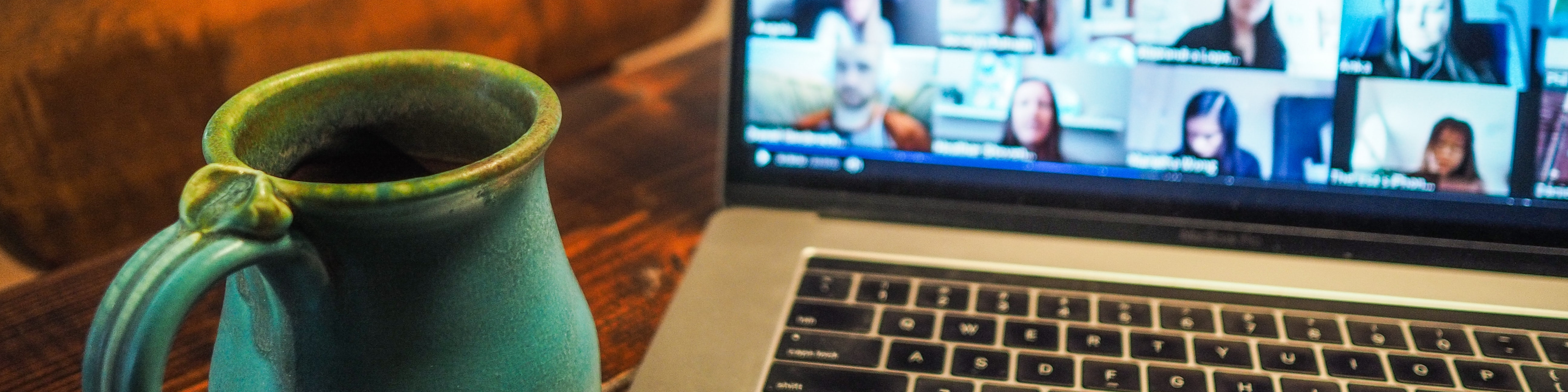 KI generiert: Das Bild zeigt einen Laptop mit einer laufenden Videokonferenz auf dem Bildschirm und eine grüne Tasse daneben. Der Hauptinhalt des Bildes ist die Darstellung einer virtuellen Besprechung oder eines Online-Meetings.