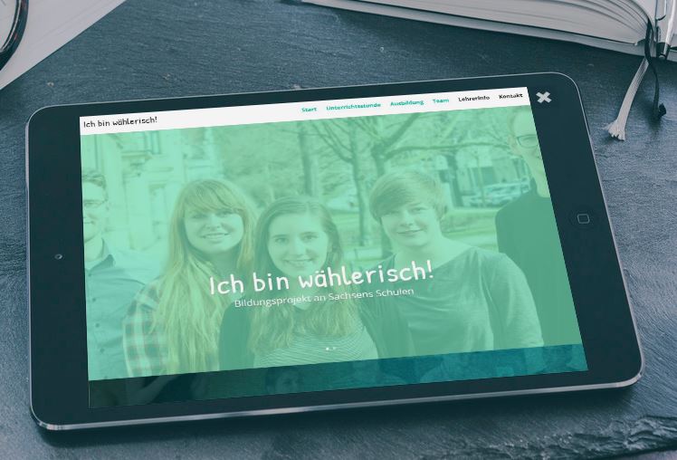 KI generiert: Das Bild zeigt ein Tablet, das auf einem Tisch liegt und eine Website mit dem Titel "Ich bin wählerisch!" anzeigt, die sich auf ein Bildungsprojekt an sächsischen Schulen bezieht. Im Hintergrund sind ein Notizbuch und ein Stift zu sehen.