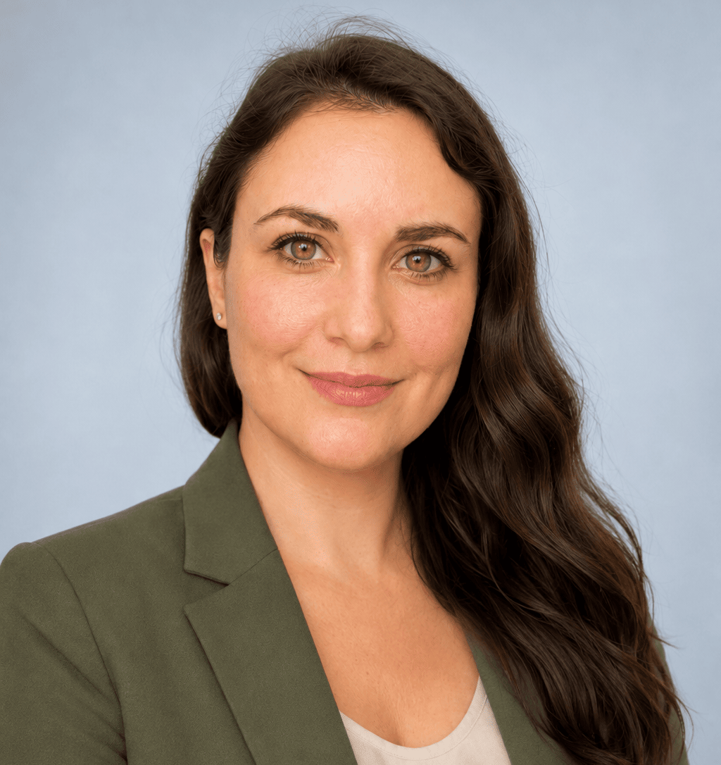 KI generiert: Das Bild zeigt eine Frau mit langen, dunklen Haaren, die einen grünen Blazer trägt und vor einem hellblauen Hintergrund steht. Der Hauptinhalt des Bildes ist ein Porträt der lächelnden Frau.