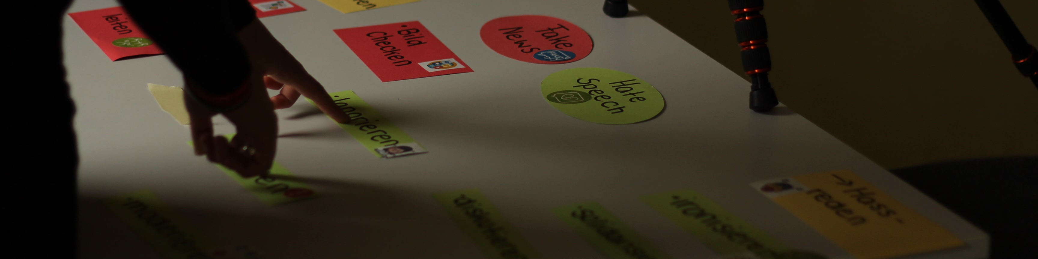 KI generiert: Das Bild zeigt eine Person, die Post-its auf einem großen Tisch oder einer Tafel anordnet, wobei die Notizen verschiedene Farben und Beschriftungen haben. Der Hauptinhalt des Bildes ist die Organisation oder Brainstorming-Sitzung, die durch die Anordnung der Notizen dargestellt wird.