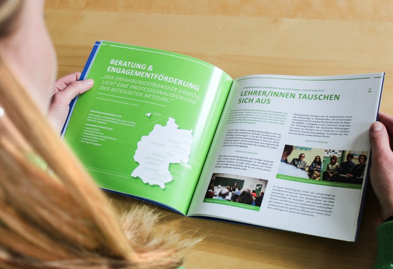 KI generiert: Das Bild zeigt eine Person von hinten, die ein aufgeschlagenes Magazin oder eine Broschüre liest. Der Hauptinhalt des Magazins scheint sich um Beratung und Engagementförderung zu drehen, mit einem Fokus auf Themen wie "Lehrer/innen tauschen sich aus" und einer Karte Deutschlands.