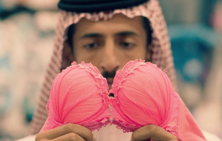 KI generiert: Das Bild zeigt eine Person, die ein pinkfarbenes Unterwäscheset vor sich hält. Die Person trägt traditionelle arabische Kleidung, einschließlich eines Kopfbedeckens.