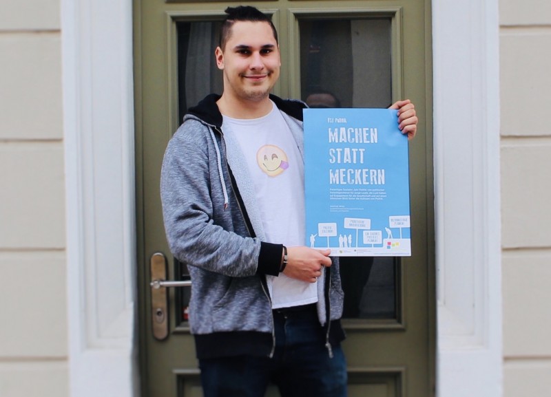 KI generiert: Das Bild zeigt einen jungen Mann, der lächelnd vor einer Tür steht und ein Plakat mit der Aufschrift "MACHEN STATT MECKERN" hält. Der Hauptinhalt des Bildes ist die positive Botschaft des Plakats, das zum Handeln statt zum Kritisieren auffordert.