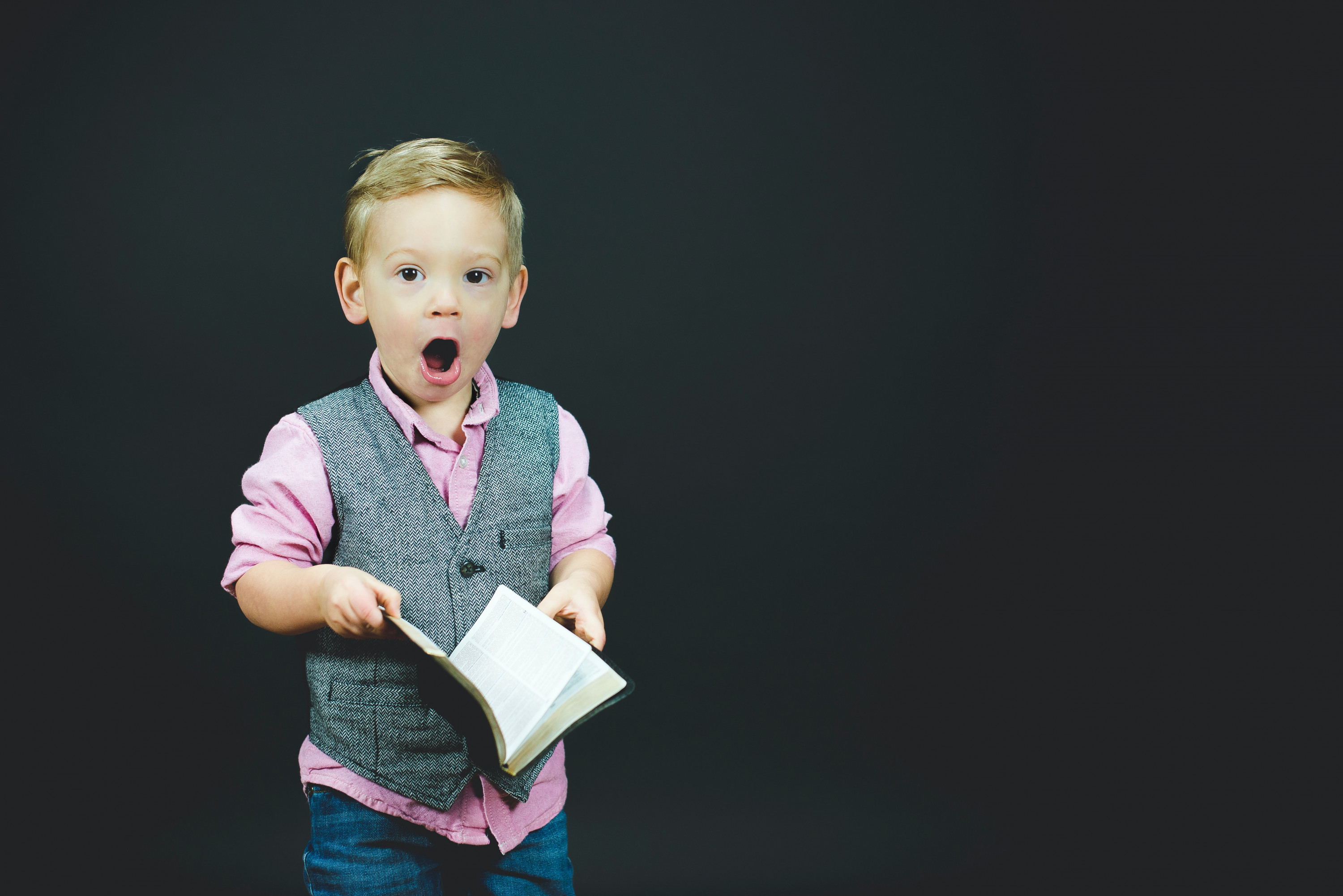 KI generiert: Das Bild zeigt einen überrascht dreinblickenden Jungen, der ein Buch in der Hand hält und formell gekleidet ist. Der Hauptinhalt des Bildes ist der Ausdruck von Überraschung oder Erstaunen des Jungen.