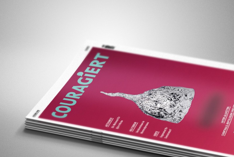KI generiert: Das Bild zeigt ein Stapel von Zeitschriften mit dem Titel "COURAGIERT" auf dem Deckblatt. Der Hauptinhalt des Bildes ist die oberste Zeitschrift, die eine auffällige Grafik eines in Alufolie eingewickelten Gegenstandes auf einem pinken Hintergrund zeigt.