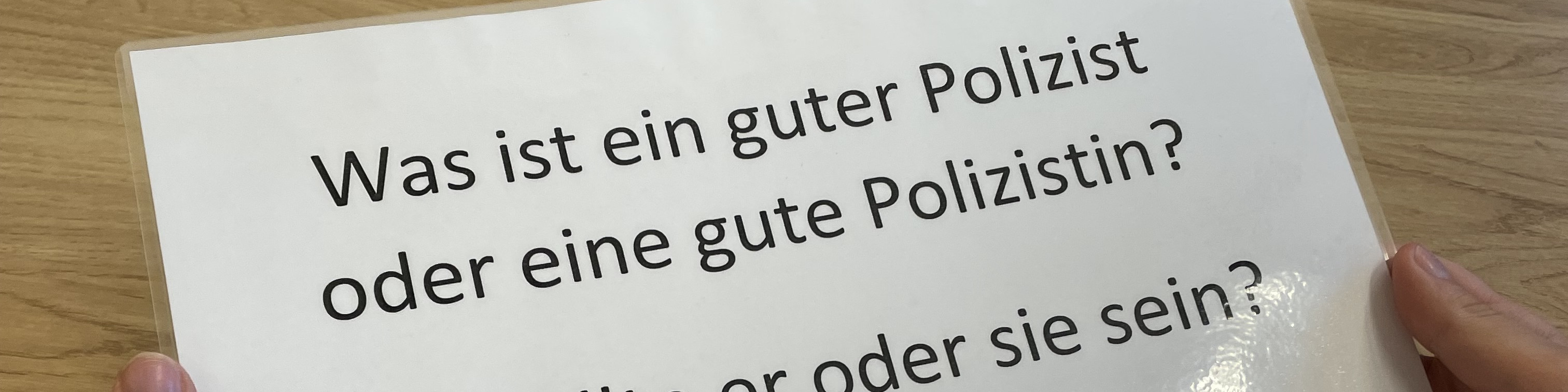 KI generiert: Das Bild zeigt eine Person, die ein weißes Blatt Papier mit der Frage "Was ist ein guter Polizist oder eine gute Polizistin? Wer oder sie sein?" hält. Der Hauptinhalt des Bildes ist die gestellte Frage auf dem Papier.