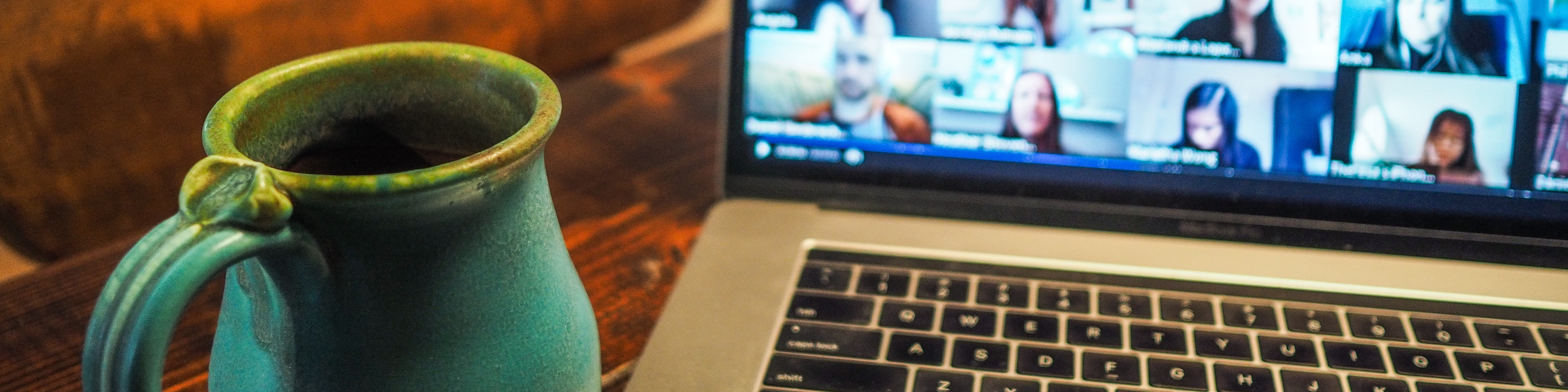 KI generiert: Das Bild zeigt einen Laptop mit einer laufenden Videokonferenz auf dem Bildschirm und eine grüne Tasse daneben. Der Hauptinhalt des Bildes ist die Darstellung einer virtuellen Besprechung oder eines Online-Meetings.