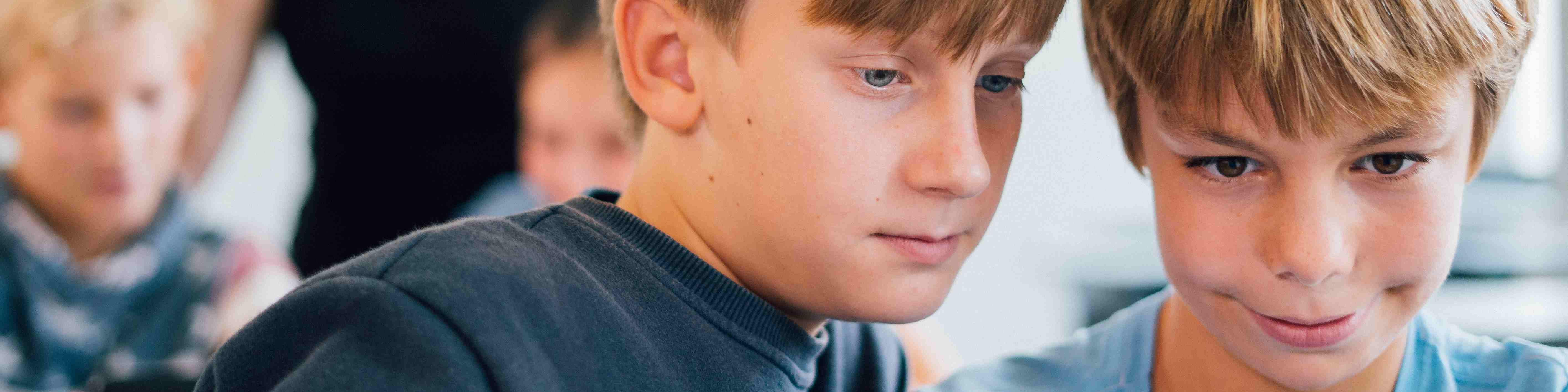 KI generiert: Das Bild zeigt zwei Jungen, die sich auf eine Aktivität oder ein Objekt konzentrieren, möglicherweise einen Laptop oder ein Buch. Der Hauptinhalt des Bildes ist die Interaktion und das gemeinsame Interesse der beiden Jungen.
