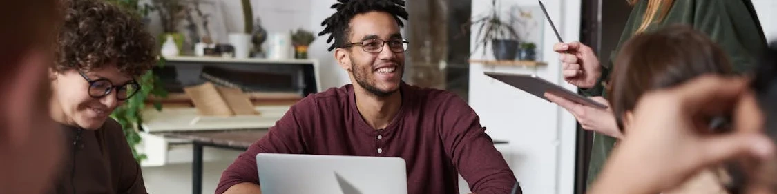 KI generiert: Das Bild zeigt eine Gruppe von Personen, die in einem modernen Büro oder Co-Working-Space zusammenarbeiten. Eine Person im Vordergrund arbeitet an einem Laptop, während andere im Hintergrund diskutieren und Notizen machen.