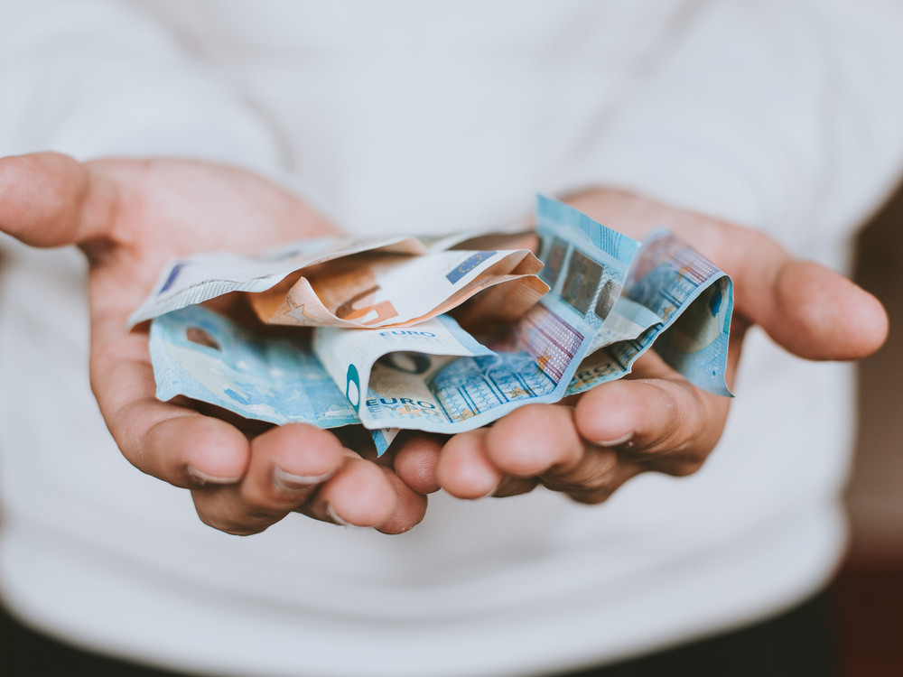 KI generiert: Das Bild zeigt zwei Hände, die mehrere zerknüllte Euro-Banknoten halten. Der Hauptinhalt des Bildes ist Geld, genauer gesagt Euro-Geldscheine.