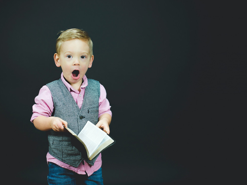 KI generiert: Das Bild zeigt einen überrascht dreinblickenden Jungen, der ein Buch in der Hand hält und formell gekleidet ist. Der Hauptinhalt des Bildes ist der Ausdruck von Überraschung oder Erstaunen des Jungen.