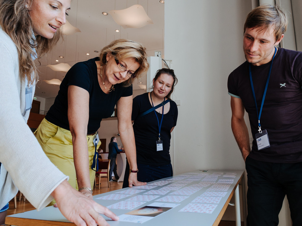 KI generiert: Das Bild zeigt eine Gruppe von Menschen, die in einem Kreis sitzen und sich in einer Diskussions- oder Arbeitsgruppe unterhalten. Der Hauptinhalt des Bildes ist eine interaktive Sitzung oder ein Workshop in einem hellen, holzgetäfelten Raum.