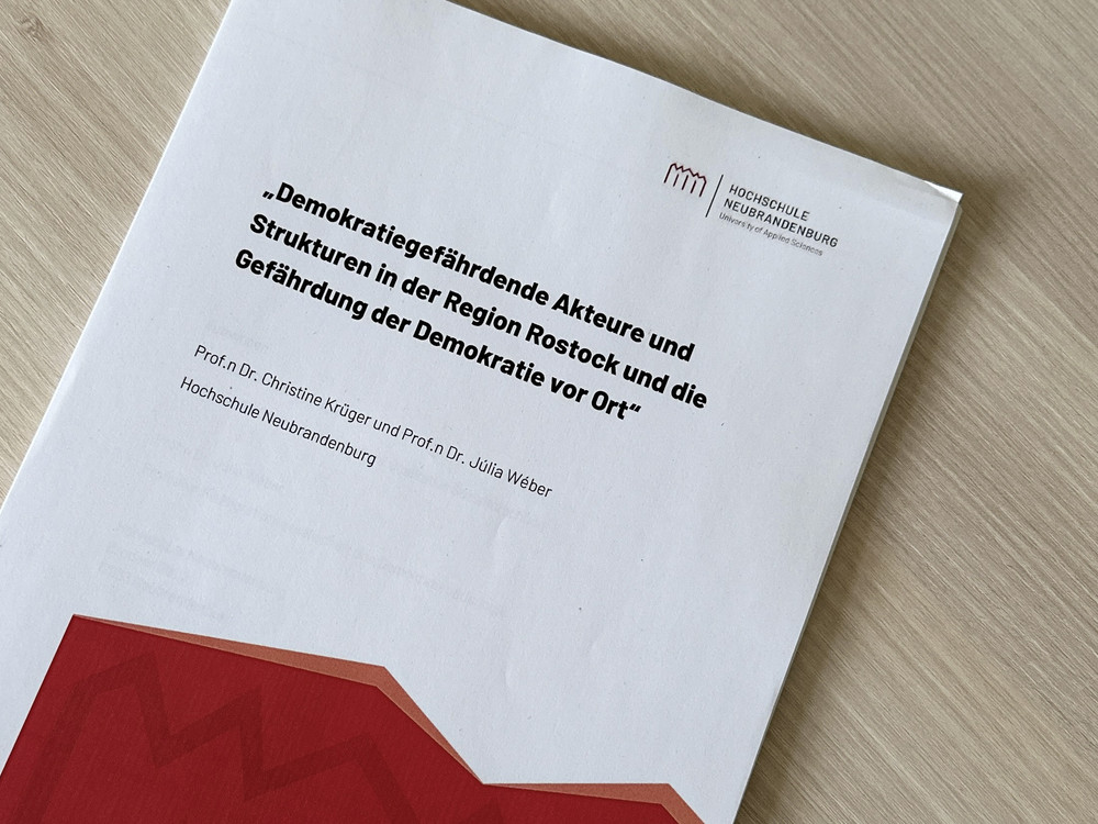 KI generiert: Das Bild zeigt die Titelseite eines Dokuments mit dem Titel "Demokratiegefährdende Akteure und Strukturen in der Region Rostock und die Gefährdung der Demokratie vor Ort". Die Autoren sind Prof.in Dr. Christine Krüger und Prof.in Dr. Julia Weber von der Hochschule Neubrandenburg.