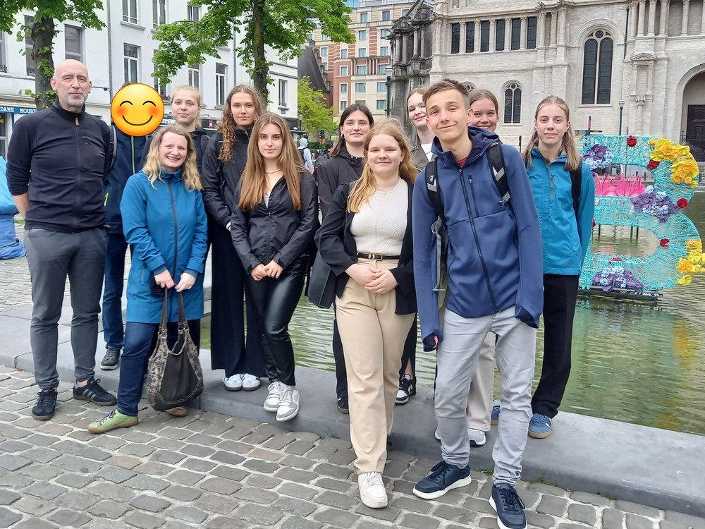 KI generiert: Das Bild zeigt eine Gruppe von Jugendlichen und einer erwachsenen Begleitperson, die vor einer Reihe von Flaggen verschiedener Länder posieren und einige von ihnen halten kleine EU-Flaggen in den Händen. Der Hauptinhalt des Bildes ist eine Gruppe von Menschen, die möglicherweise an einem internationalen oder europäischen Event teilnehmen.