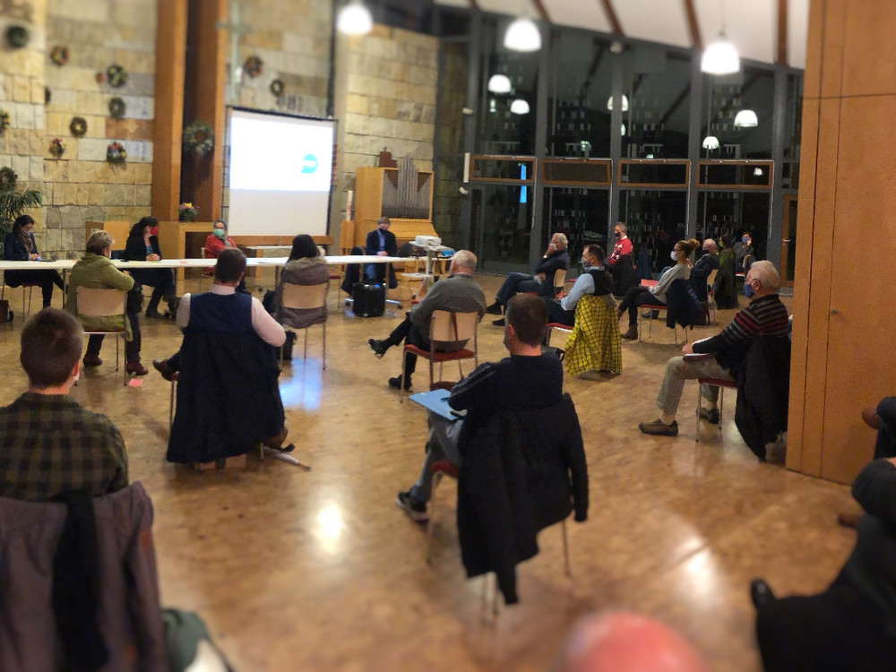 KI generiert: Das Bild zeigt eine Gruppe von Personen, die in einem großen, rustikalen Raum mit Holzboden und Steinwänden an einem Seminar oder einer Präsentation teilnehmen. Der Hauptinhalt ist eine Bildungsveranstaltung, bei der eine Person vorne präsentiert und die anderen zuhören.