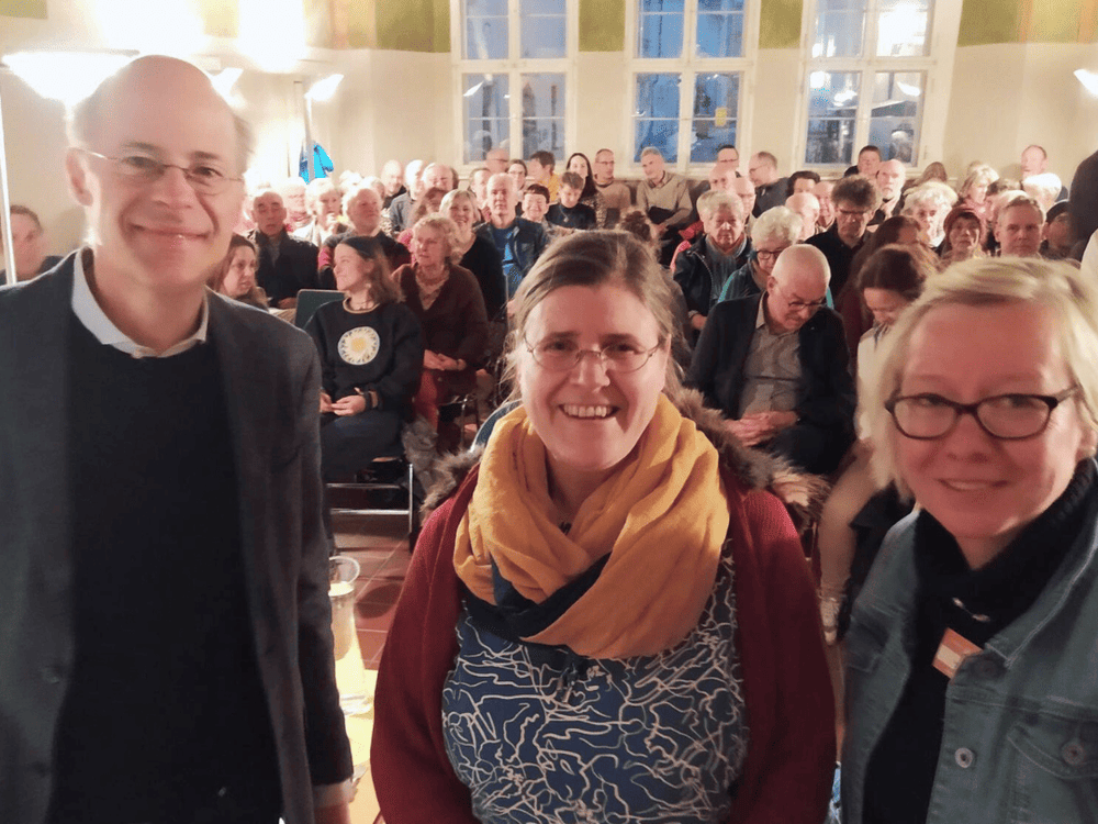 KI generiert: Das Bild zeigt eine große Gruppe von Menschen, die in einem Raum sitzen und einer Veranstaltung oder Präsentation zuhören. Der Hauptinhalt des Bildes ist eine aufmerksame Zuhörerschaft in einer Versammlungs- oder Vortragssituation.
